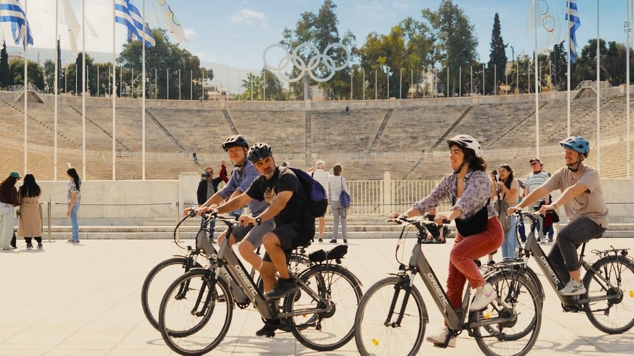 A group on e-bikes rides past the marble seats of the Panathenaic Stadium on an Athens bike tour