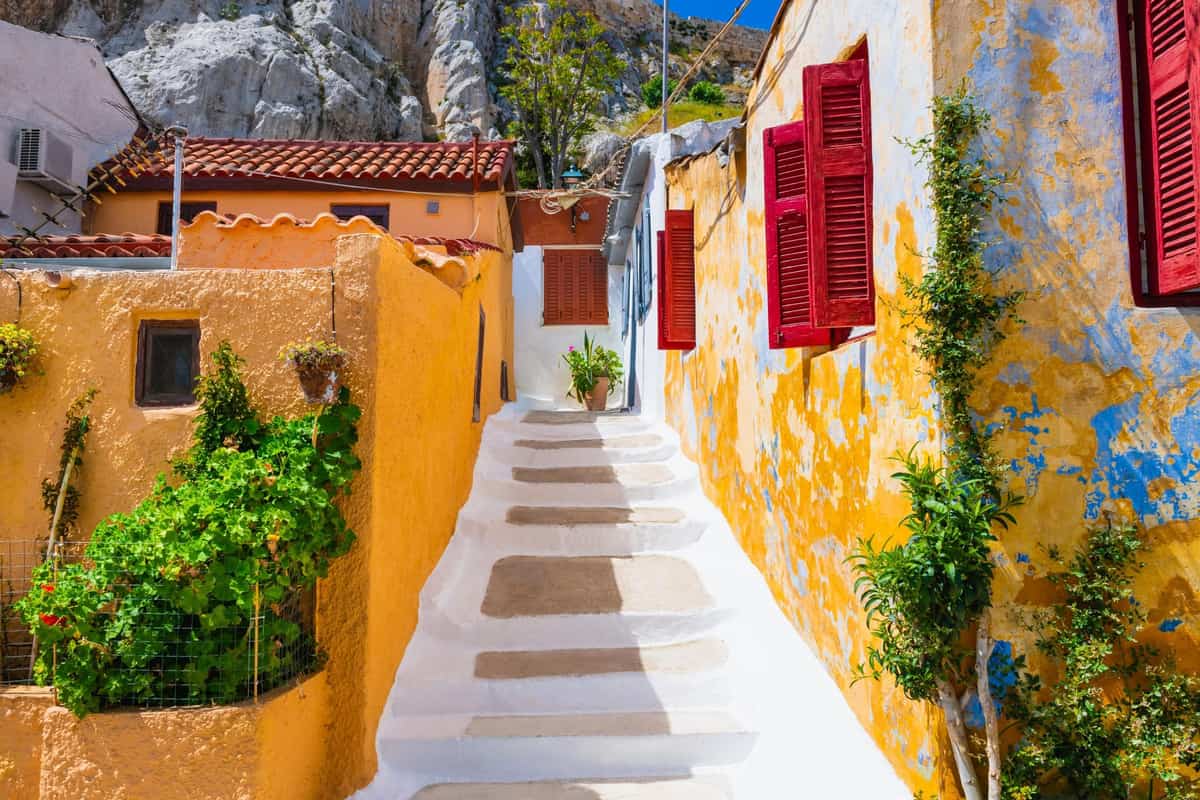 Whitewashed steps climb a narrow lane between yellow houses with red shutters below the Acropolis rock on an Athens walking tour