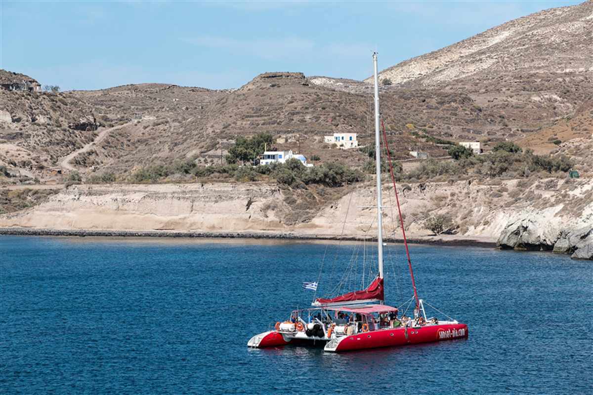 A red sailing catamaran at anchor in a calm Greek bay