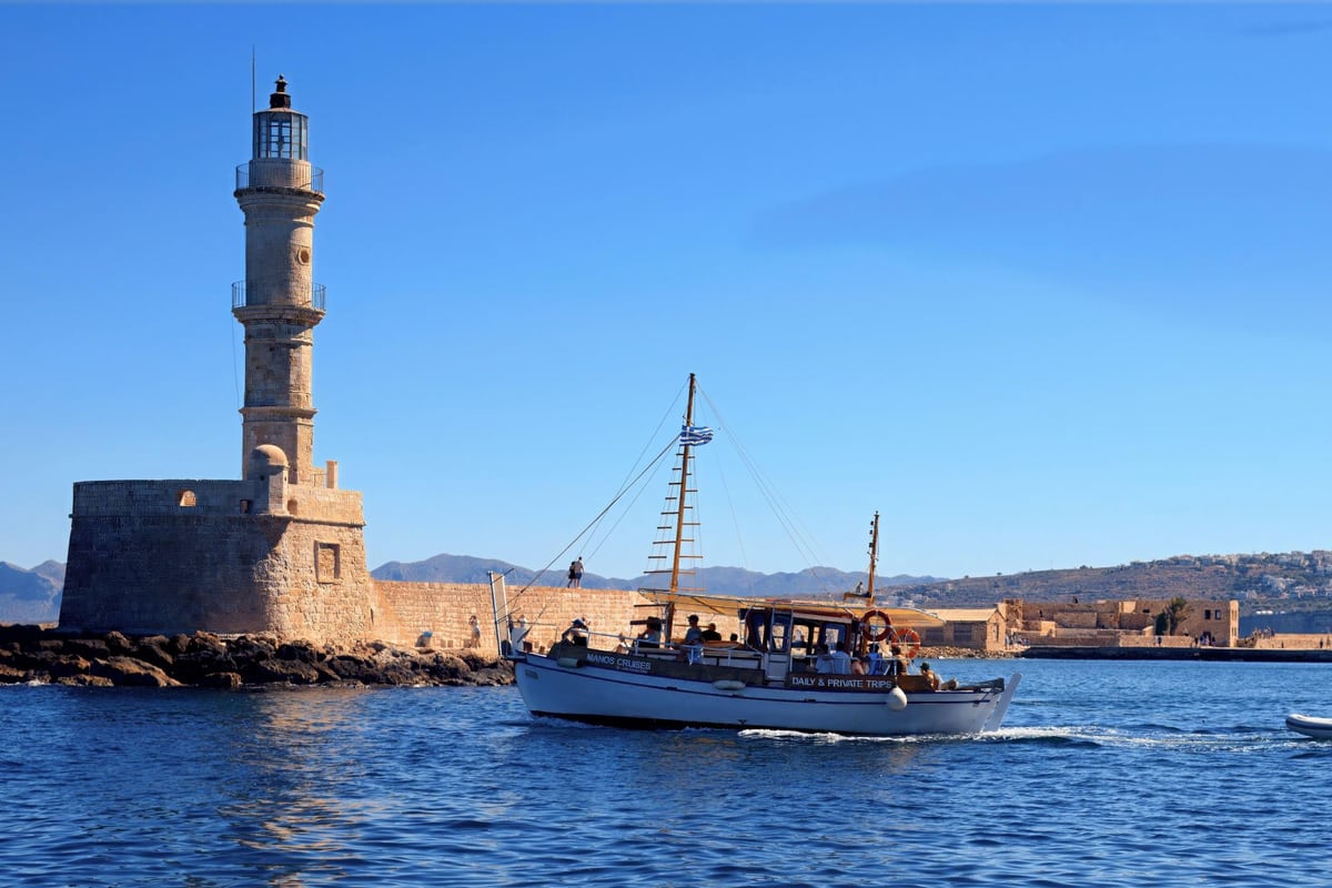 A wooden tour boat sails past the Venetian lighthouse of the old harbour on a Chania boat trip
