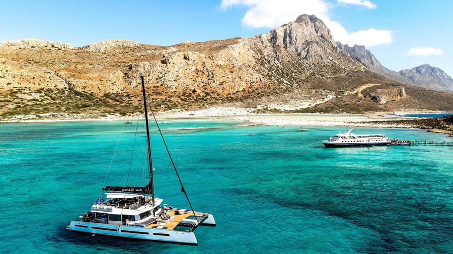 A catamaran anchored in the turquoise water of Balos lagoon below Cape Gramvousa on a Chania boat trip