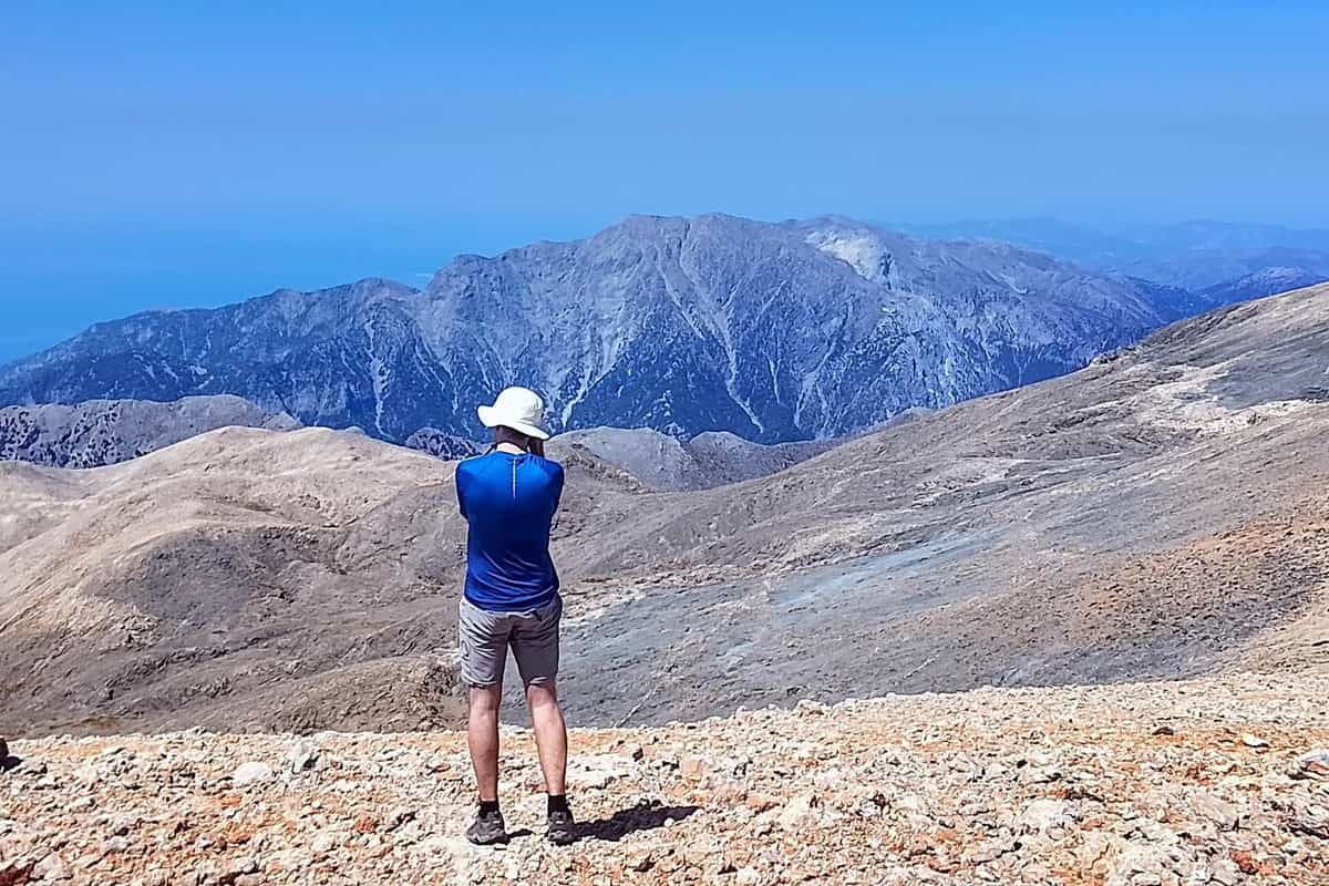 A hiker on a high stony ridge looks across to the bare peaks of the White Mountains on a Chania hiking tour