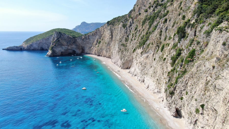 White cliffs above a long beach and clear water on the west coast seen on a Corfu boat trip