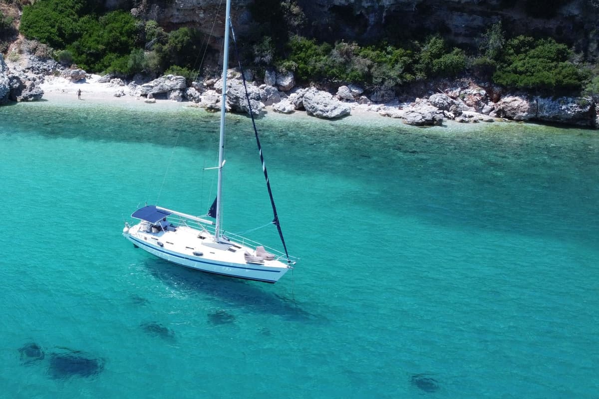 Sailboat at anchor in a turquoise bay below green cliffs, a Corfu sailing tour on the Ionian coast