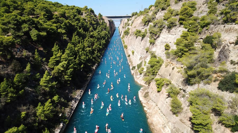 Dozens of paddleboarders move along the narrow blue channel between pine-topped walls on a Corinth canal tour