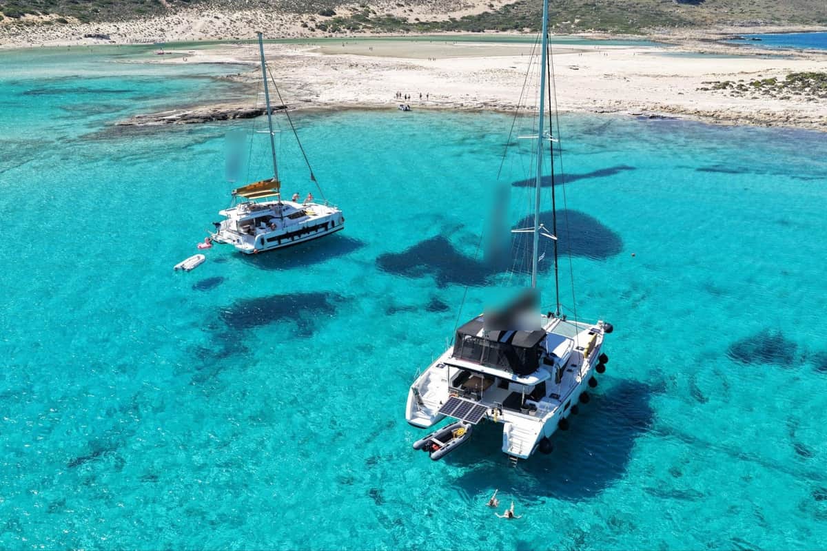 Two sailing catamarans anchored in the turquoise water of Balos lagoon on a Crete catamaran cruise