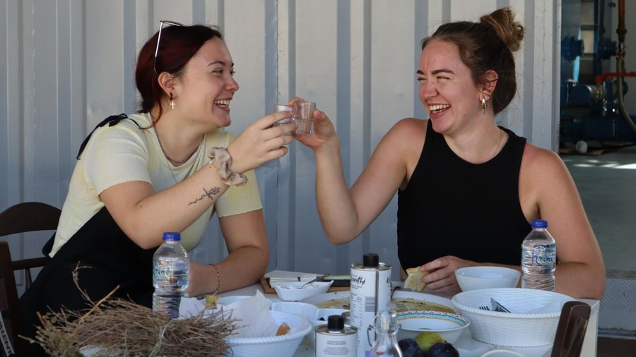 Two visitors laugh as they taste olive oil and local food at a farm table on a Crete olive oil tour