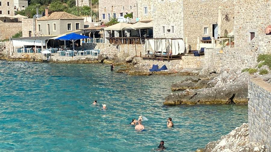 Stone houses above clear water in the bay of Limeni, a stop that follows a Diros caves tour