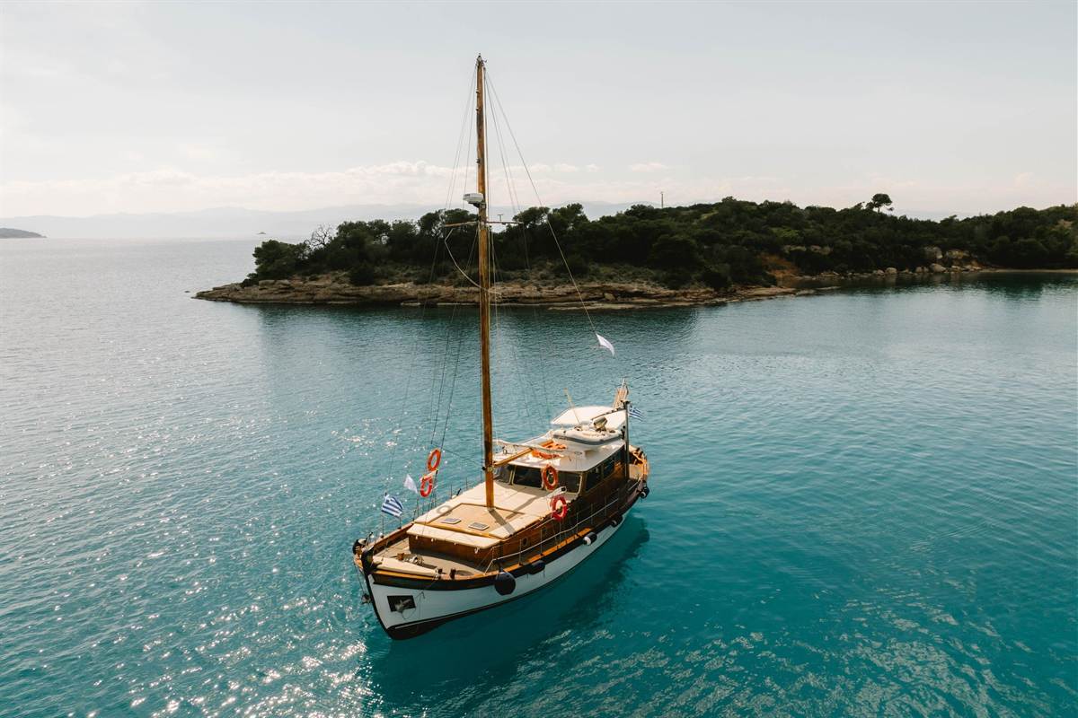 A wooden boat moored by a pine-covered islet in calm water, the kind of boat used on an Ermioni boat trip