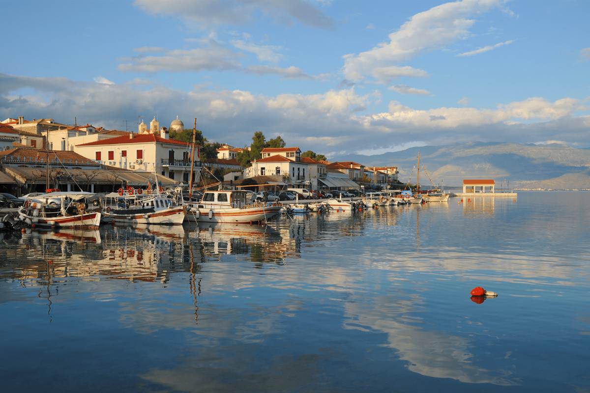 The harbour of Galaxidi with boats and old houses reflected in calm water, the start of a Galaxidi day trip