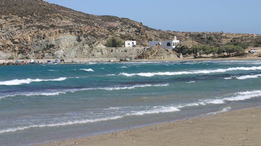 Sandy Paros beach with white surf and a hillside chapel above the sea
