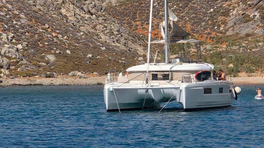 A sailing catamaran lies at anchor in a calm bay below rocky slopes on a Heraklion sailing tour