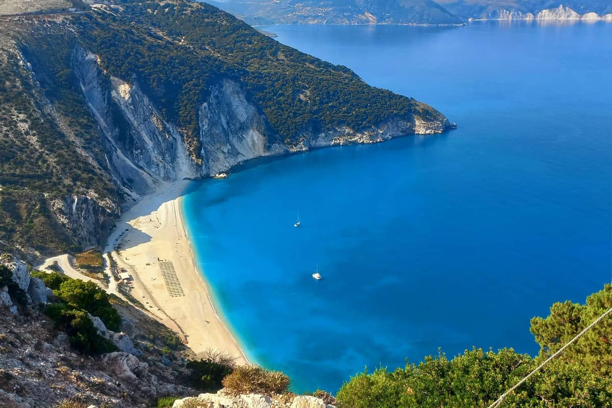 The white crescent of Myrtos beach and deep blue water below steep cliffs, seen from the road on a Kefalonia island tour