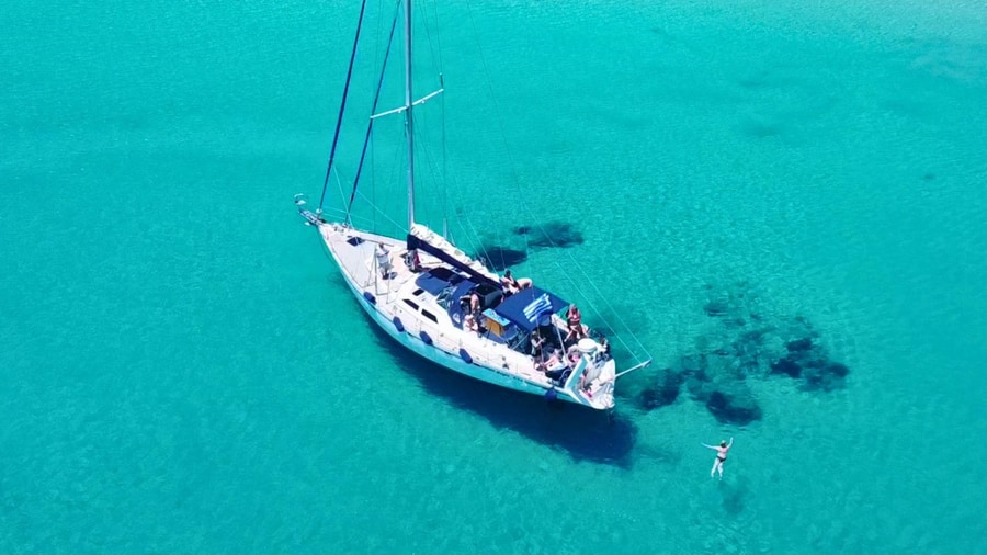 A sailing yacht at anchor in shallow turquoise water with a swimmer nearby on a Kos boat trip