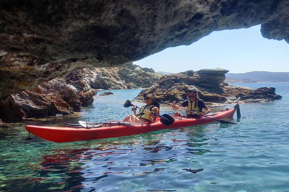 Kayaks passing under a rock arch over clear water on Kythnos, a format of a Kythnos boat trip
