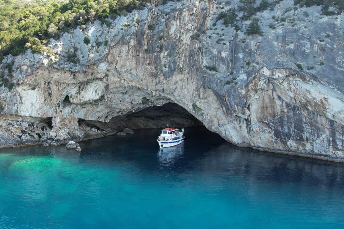 A white tour boat waits at the mouth of a huge sea cave under grey cliffs on a Lefkada boat tour