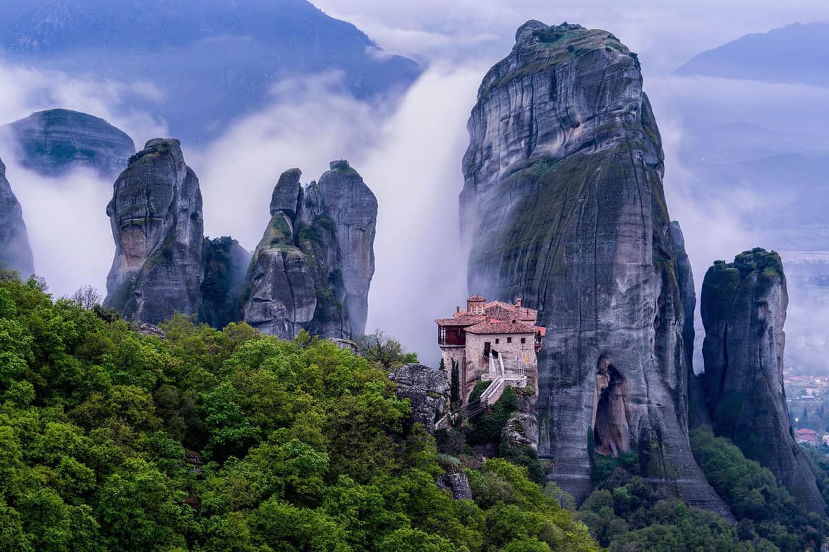Rock pillars and a monastery in the mist above green hills, the sight of a Meteora day trip from Athens