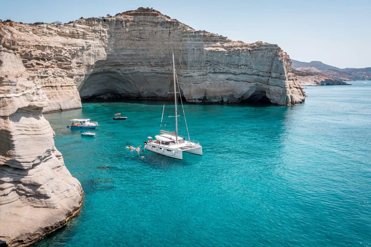 A sailboat in the turquoise water below the white cliffs of Kleftiko on a Milos sailing tour
