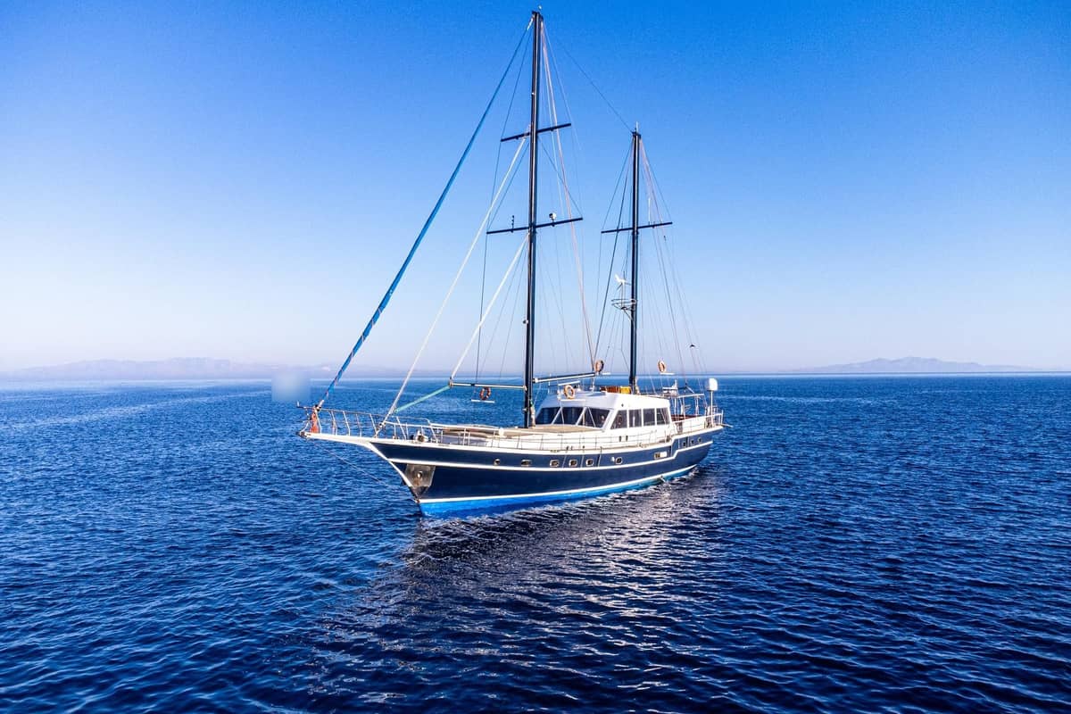 A navy-hulled two-masted yacht cruises on calm deep-blue water on a Mykonos yacht cruise to Delos and Rhenia
