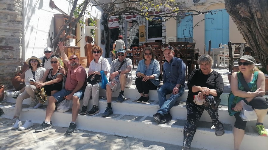 A tour group rests on whitewashed steps in the shaded village square of Halki on a Naxos tour