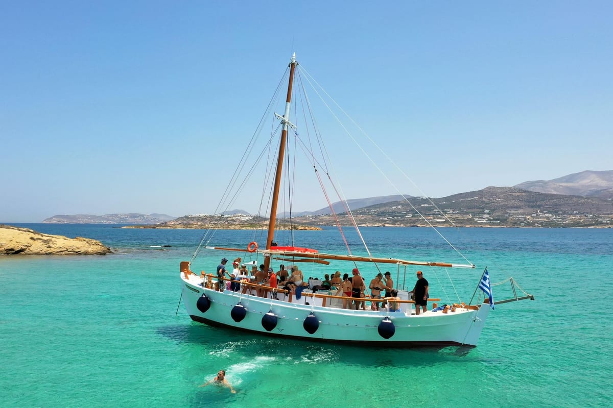 A swimmer dives off a white wooden caique anchored in turquoise water between Paros and Antiparos on a Paros snorkeling trip