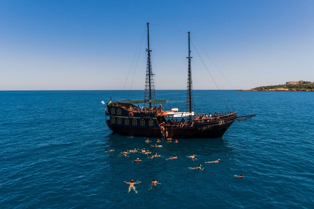 A pirate-style Rethymno boat trip ship at anchor on deep blue water while swimmers take a swim stop beside it