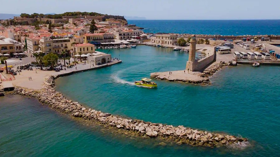 A speedboat leaves the Venetian harbour and lighthouse of Rethymno on a boat trip over turquoise water