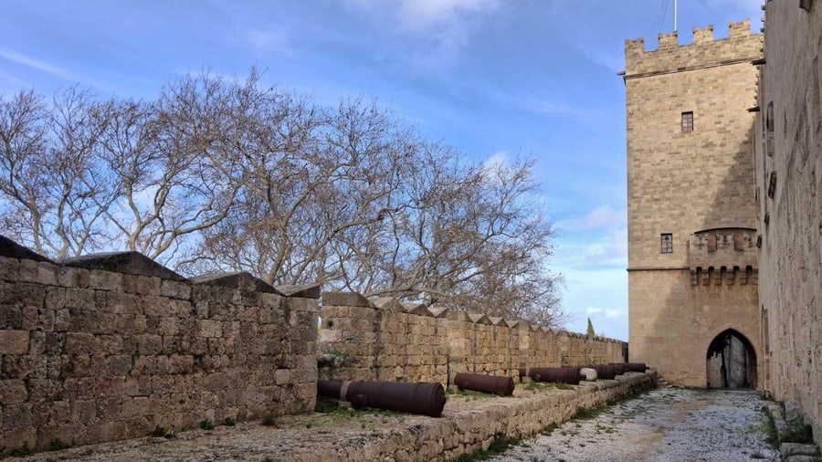 Old cannons line a stone rampart beside a tower, a quiet stop on a Rhodes old town tour
