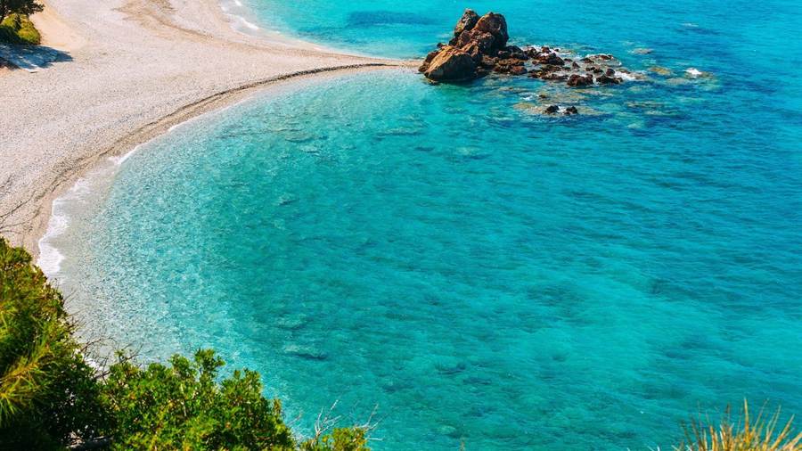 A sandy beach and a rock in turquoise water on the coast of Samos, a stop on a Samos boat trip