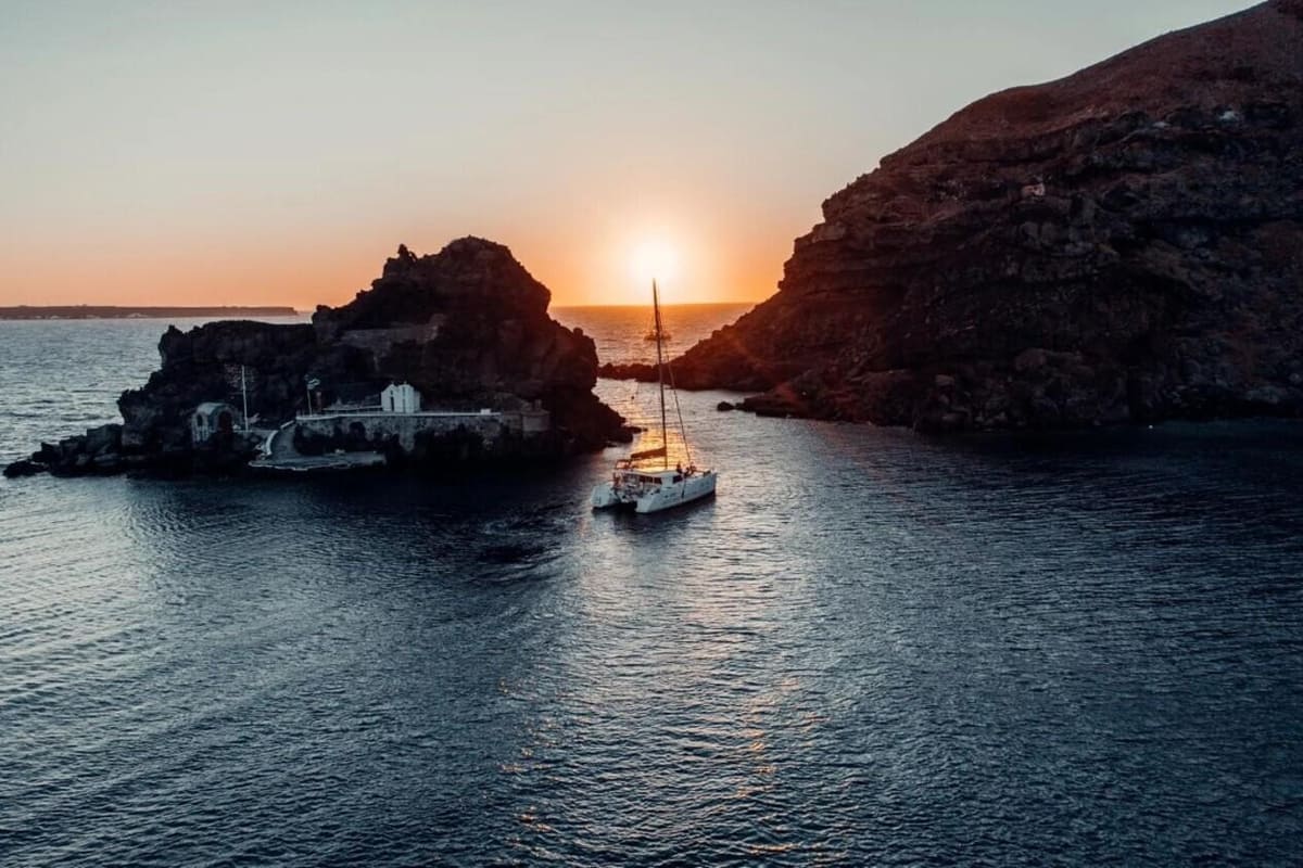 A sailing catamaran at sunset by the rocks off Oia on a Santorini boat tour