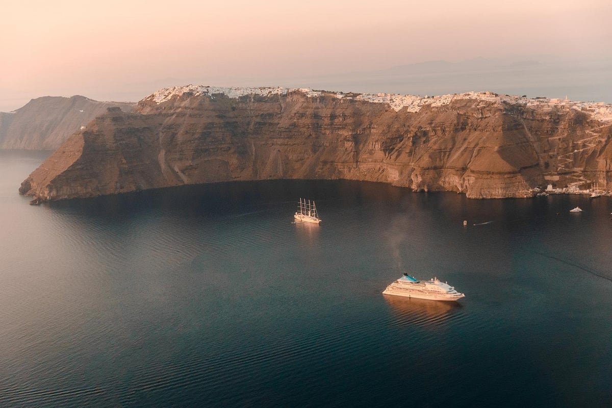 The caldera wall of Santorini with two boats on the water, seen on a Santorini catamaran cruise