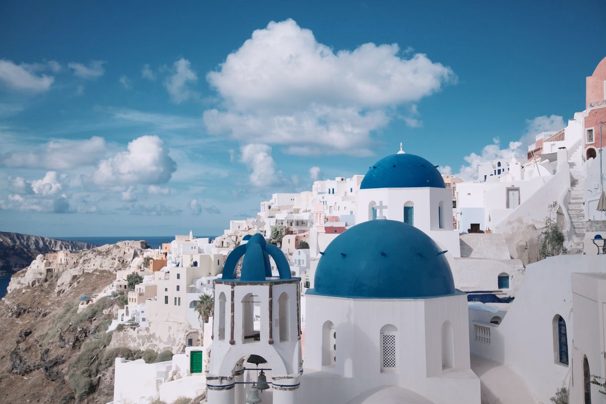 Blue-domed churches and white houses of Oia above the caldera under a bright sky, a classic stop on a Santorini private tour