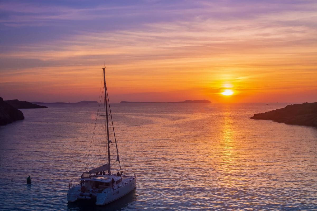 A catamaran sits on the calm caldera sea as the sun sets in an orange sky on a Santorini sunset tour