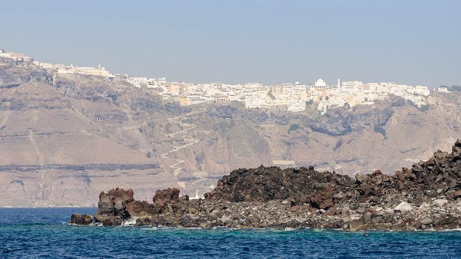 Fira on the caldera rim above the dark lava of Nea Kameni, seen on Santorini tours