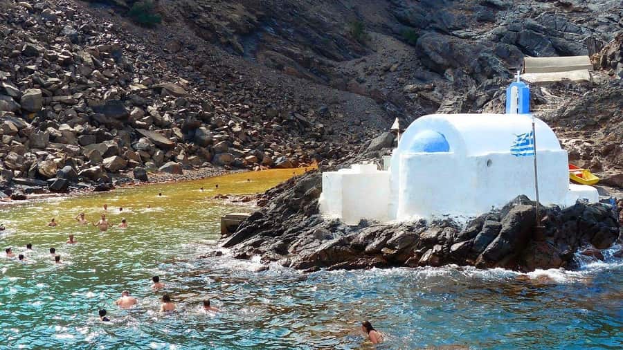 A small white chapel on the lava shore of the hot springs bay on a Santorini volcano tour