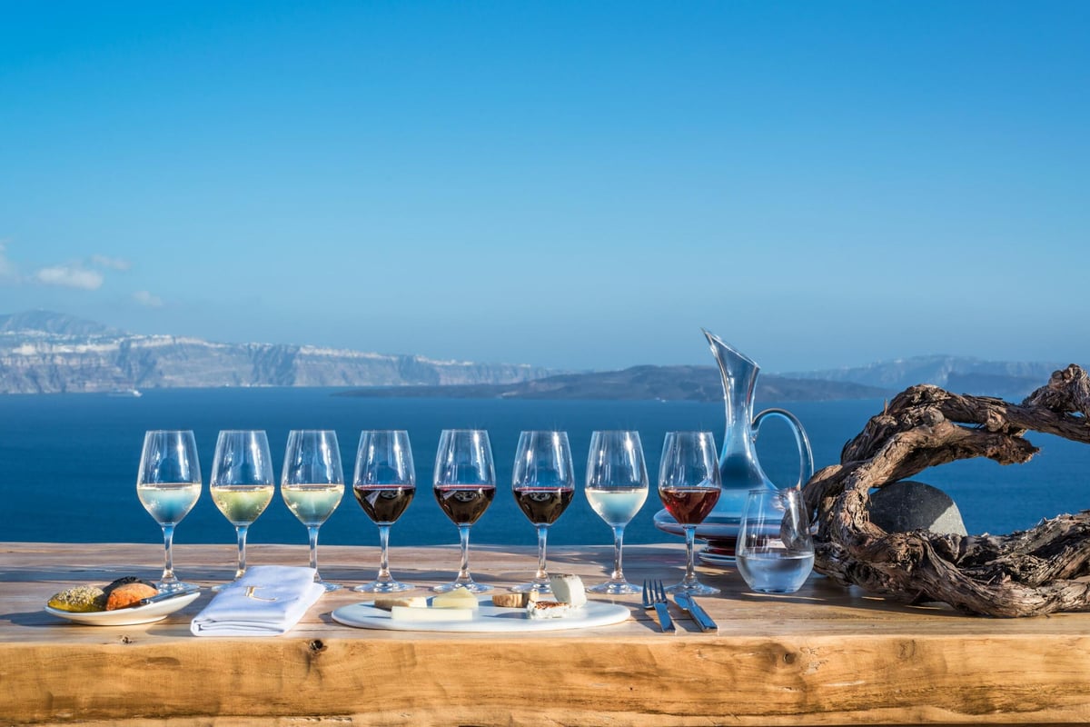 A row of tasting glasses of white, rose and red wine on a table above the caldera sea on a Santorini wine tour