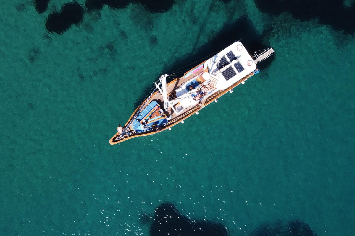 A wooden excursion boat lies at anchor over clear turquoise water, seen from above, on a Skiathos boat trip