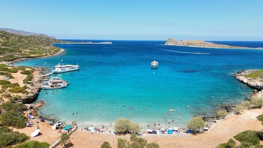 A turquoise bay with boats on the sea route of a Spinalonga tour
