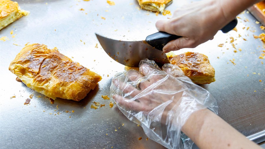 Hands cutting fresh bougatsa pastry on a metal tray, the morning stop of a Thessaloniki food tour