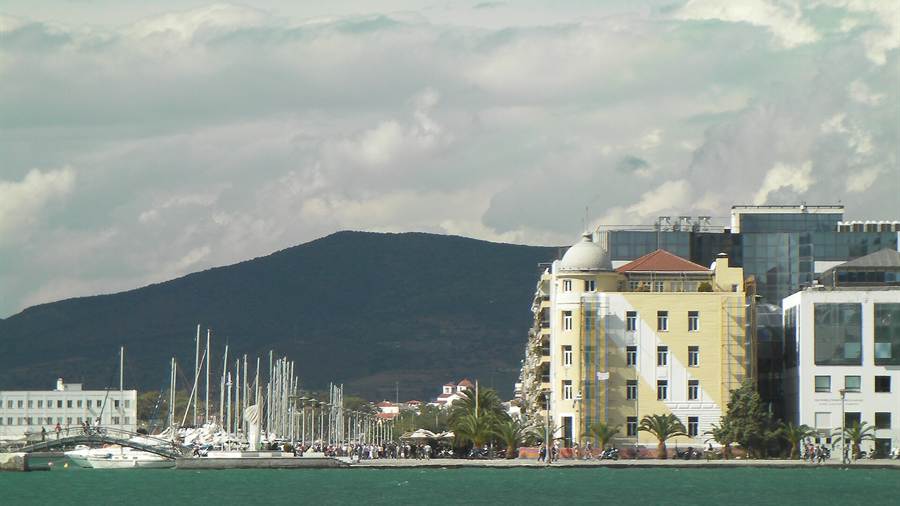 Marina and seafront buildings of Volos below a green mountain slope